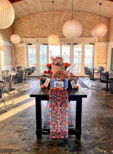 A decorated banquet room with hanging globe lights, arranged chairs, and a long table set with food and colorful runner.