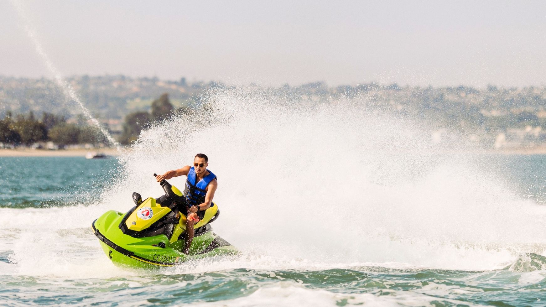 A man speeds across the ocean on a bright green jet ski, kicking up a huge spray behind him.