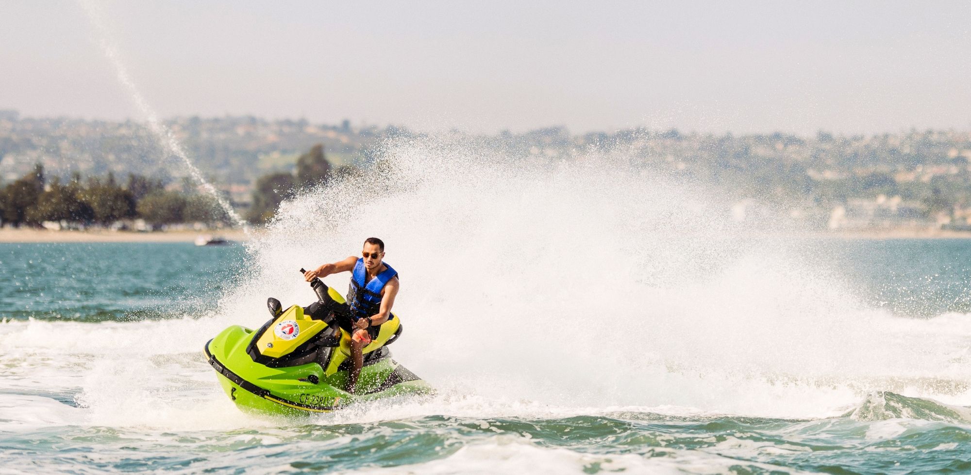 A man speeds across the ocean on a bright green jet ski, kicking up a huge spray behind him.