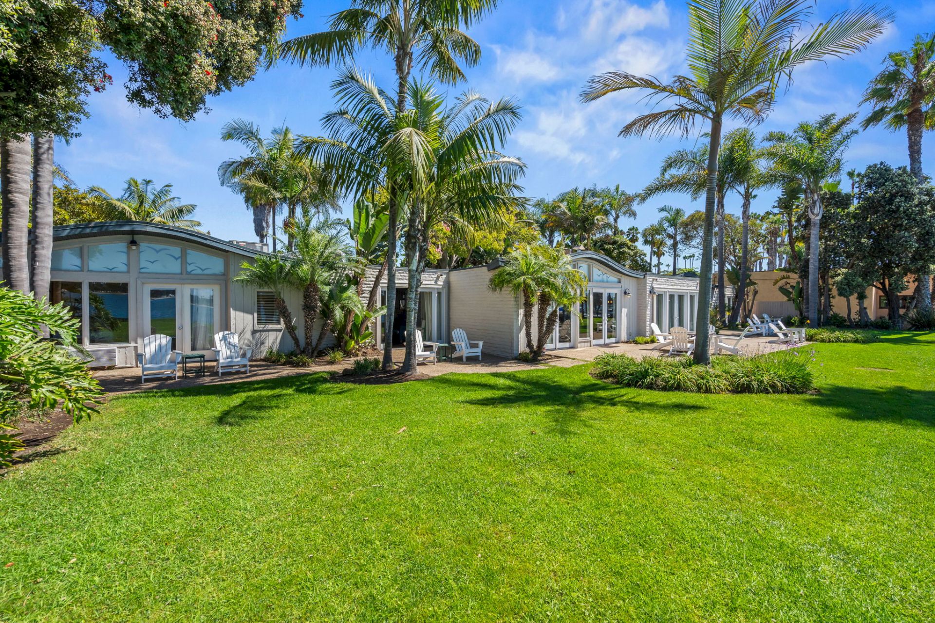 Tropical resort courtyard with palm trees, a manicured green lawn, and white cottage patios under a bright blue sky.