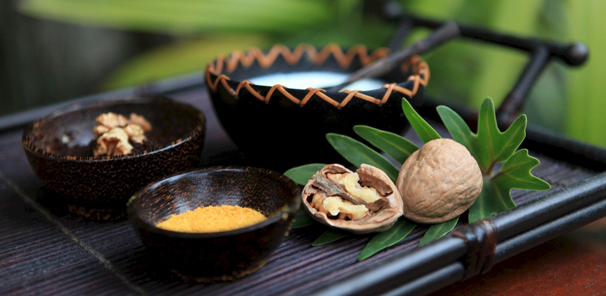 A grill scene with spiced skewers, bowls of seasoning, and walnuts with fresh green leaves on a dark metal rack.