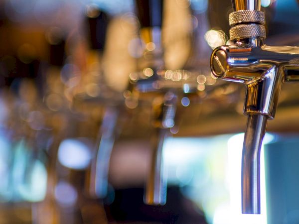 A close-up of a shiny chrome beer tap with a blurred bar background and bokeh lights.