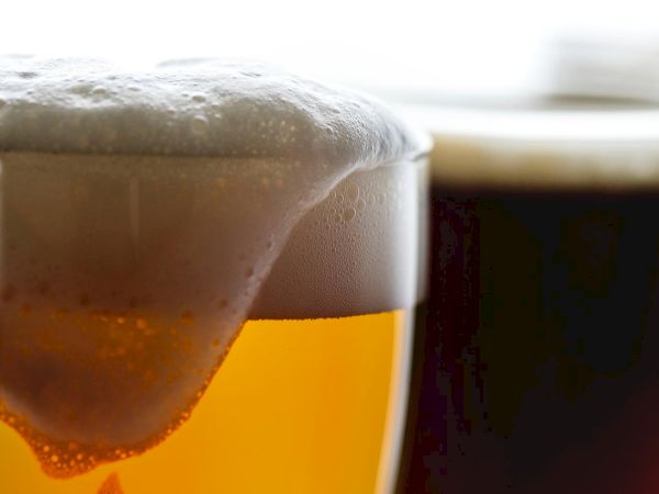 Close-up of a foamy beer glass with condensation and bubbles rising in amber liquid beneath the head.