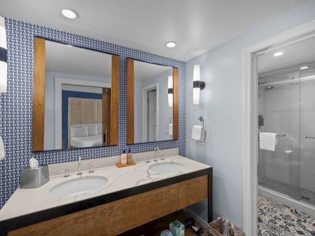A modern bathroom with a double vanity, patterned blue tile wall, large mirrors, and a glass shower.