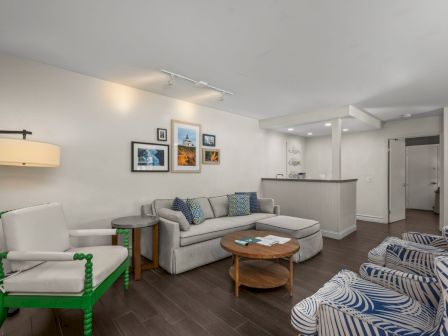 A bright modern living room with a gray sectional, green accent chair, patterned armchairs, coffee table, and framed wall art.