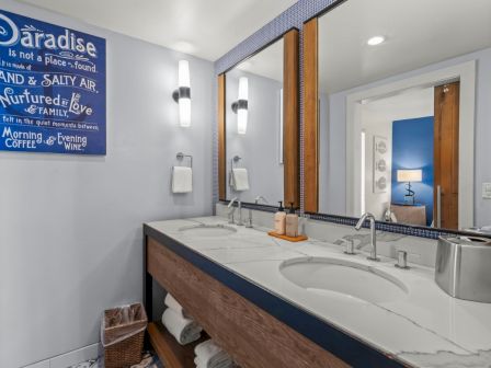 A modern bathroom with a double-sink marble vanity, wall mirrors, and a blue &ldquo;Paradise&rdquo; sign.