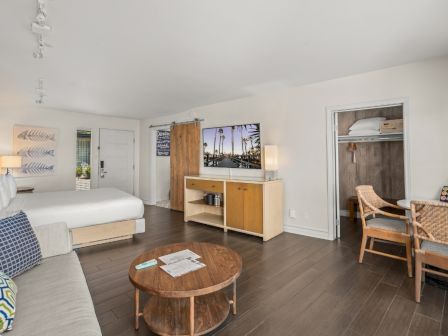 A bright hotel room with a bed, a vanity/coffee station, and a doorway leading to a small seating area.