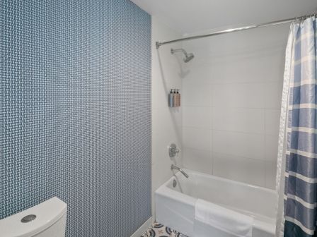 A small bathroom with a bathtub, showerhead, blue-and-white curtain, tiled walls, and a toilet.