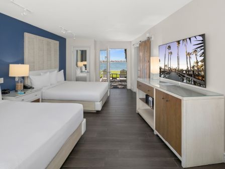 A modern seaside hotel room with twin beds, ocean view doors, and a palm photo on the wall.