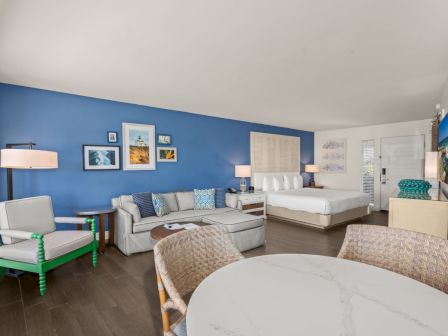 A modern bedroom with a blue accent wall, sofas, a large bed, lamps, and coastal-style wall art.