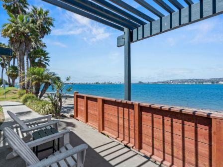 Oceanfront patio with wooden railing, Adirondack chairs, and palm trees under a bright blue sky.