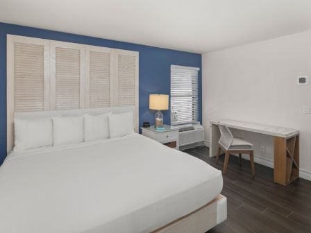 Bright bedroom with a big bed, lamp, AC unit, desk and chair, and windows showing a seaside view.