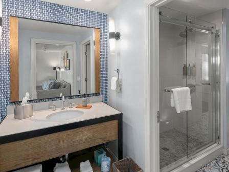 Modern bathroom with double vanity, patterned accent wall, and a glass shower with neatly folded towels.
