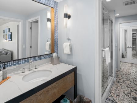 A modern bathroom with a double sink vanity, wall-mounted lights, tiled walls, and a patterned tile floor.