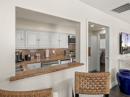 Bright kitchen with white cabinets and granite counters, a built-in coffee station, stove, and a doorway into an adjacent room.