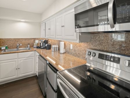 A modern kitchen with white cabinets, granite countertops, a sink, a stainless stove, and a coffee maker.