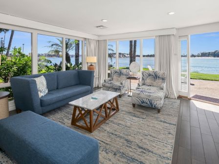 A bright, modern living room with blue sofas, patterned armchairs, a marble coffee table, and large windows overlooking the ocean, .