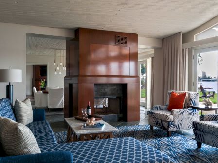 A modern living room with patterned sofas, a stone coffee table, and a built-in fireplace, plus large windows and curtains.