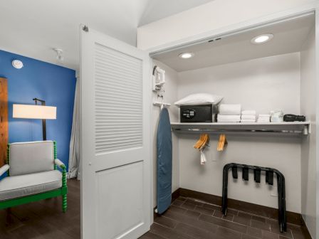 A small room with built-in cabinets, folded linens, a safe, and a chair by a blue accent wall.