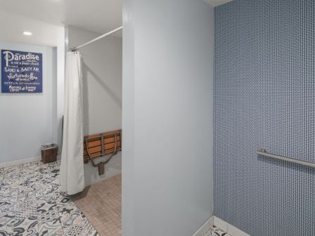 A bright bathroom with a shower curtain, tiled patterned floor, wall art, and blue textured walls around the sink area.