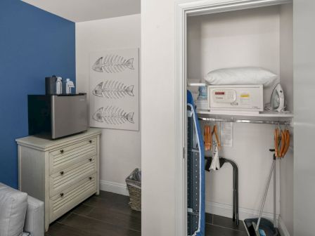 A tidy utility room with a mini-fridge, ironing setup, and an open cabinet holding supplies and tools.