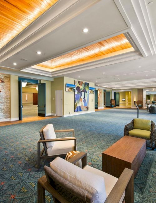 A modern hotel lounge with sofas, chairs, coffee tables, colorful wall art, and bright recessed lighting.
