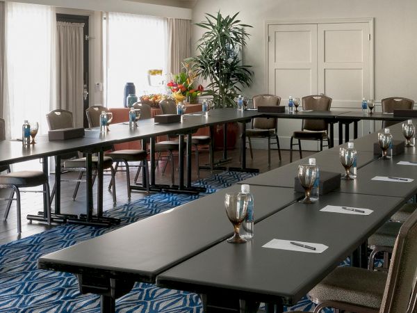 A long banquet-style conference room with chairs, place settings, and a floral centerpiece near large windows.