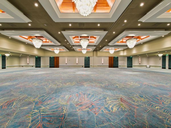 A spacious event hall with patterned carpet, green doors, and multiple chandeliers beneath warm wooden ceiling beams.