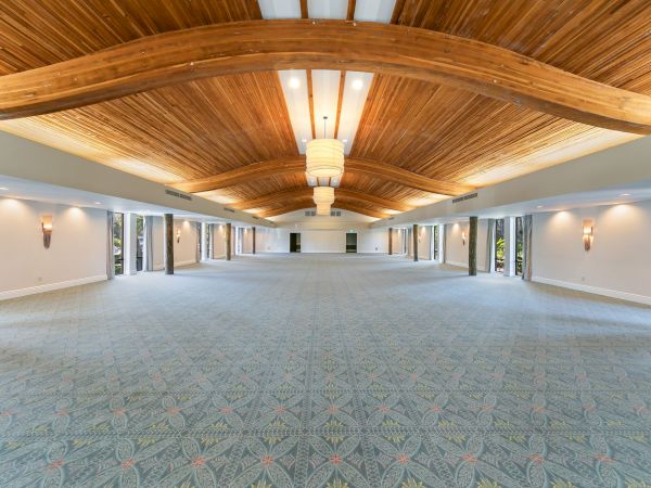 A spacious event room with a vaulted wooden ceiling, hanging lantern-style lights, patterned carpet, and glass doors opening to outdoors.