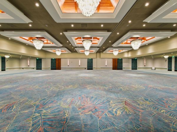 Spacious modern event hall with patterned carpet, spotlights, and crystal chandeliers under a wooden coffered ceiling.