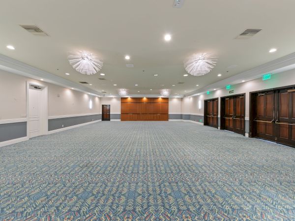 An empty, modern conference room with patterned carpet, recessed lights, ceiling fans, and several brown doors with EXIT signs.
