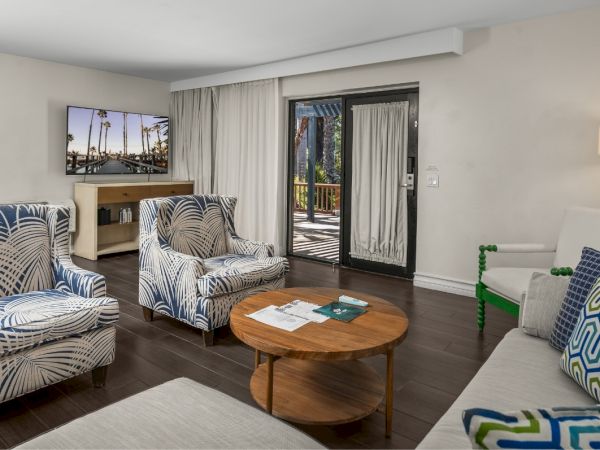 A bright living room with striped sofas, a round wooden coffee table, and an open door to a sunny balcony.