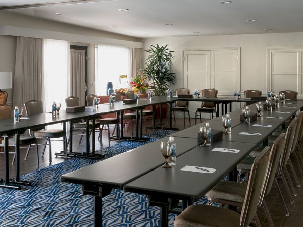 A bright conference room with long banquet-style tables, place settings, water bottles, and chairs arranged for a meeting.