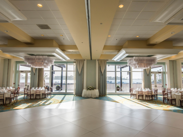 A lavish event hall set for a wedding, with round chandeliers, draped columns, and rows of banquet chairs and tables.