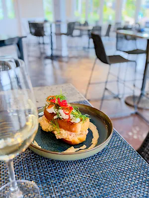 A plated appetizer with bread topped by sprouts and red peppers on a blue dish in a bright restaurant setting, ready to enjoy.