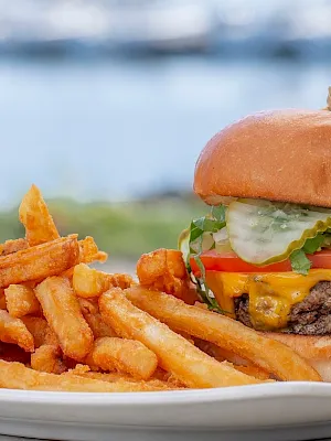 Cheeseburger with lettuce, tomato, cheese and fries on a plate in front of a beach.