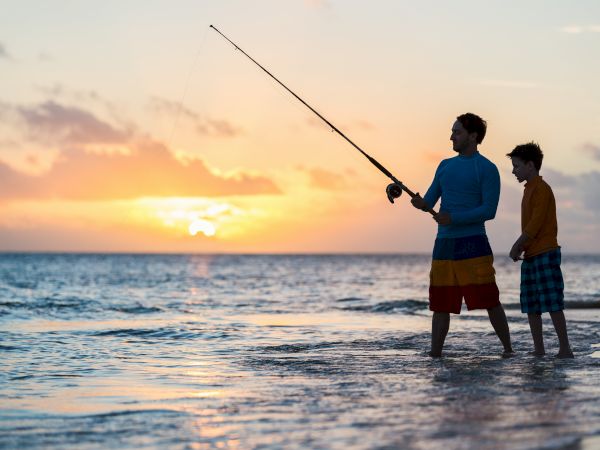 Two people fly a kite on a beach at sunset, stretching its line across the sky.
