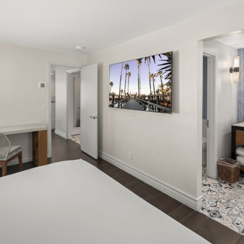 Bright hotel bathroom with double sinks, patterned tile, bench area, and a palm-tree wall photo.