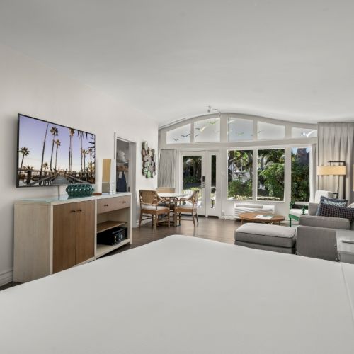 A modern living room with a white sofa, large windows, coffee table, and a bedroom-style cabinet.