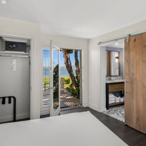 A bright coastal suite with an open door, ocean view, wooden wardrobe, and a glimpse of the bathroom vanity.