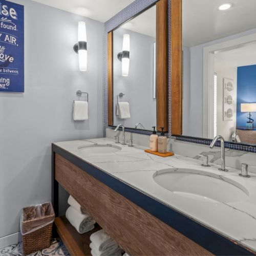 A bright bathroom with a double-sink marble vanity, towel racks, mirrors, and wall decor.