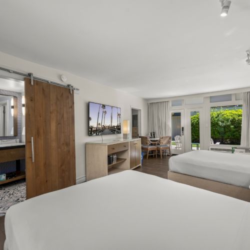 A modern hotel suite with a large bed, vanity, and an open bathroom doorway, lit by ceiling spotlights.