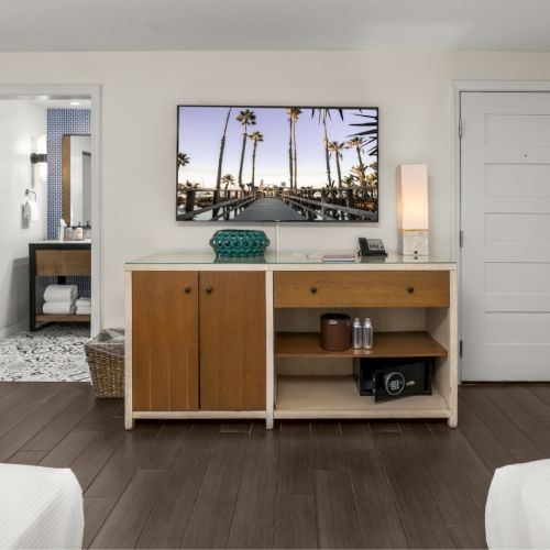 A modern hotel room: white desk vanity with wood drawers, minibar, and a palm-tree wall photo.