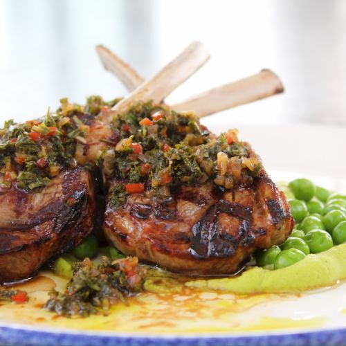 Plate of lamb chops topped with chopped herbs and veggies, served with peas and mashed potato pur&eacute;e, ready to eat.