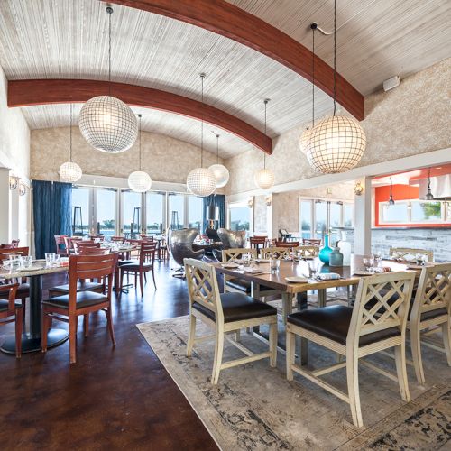 Bright restaurant dining room with wooden tables, chairs, and spherical pendant lamps, plus an open buffet kitchen area.