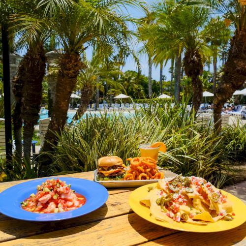 Poolside oasis with palm trees and a sunny table of tacos, nachos, and drinks by the pool.