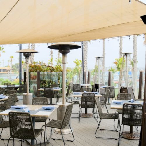 A blurry outdoor patio with benches and tables under a beige awning, showing a garden-like yard in the background.