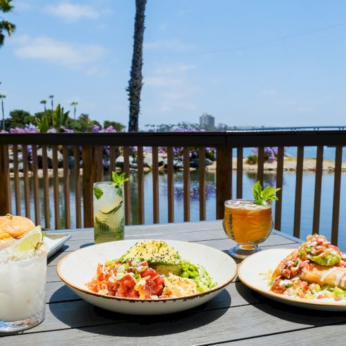 Sunny lakeside patio with colorful plates and cocktails on a table behind a wooden fence with purple flowers in bloom.