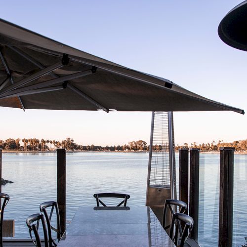 A quiet lakeside patio with umbrella, chairs, and a swing dock view at sunset.