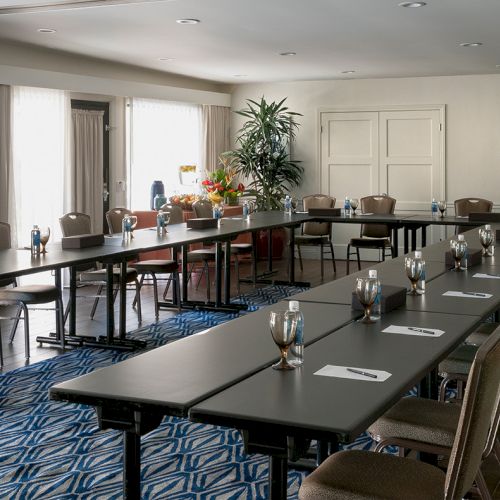 A modern meeting room set with long tables, chairs, water glasses, and napkins for a conference.